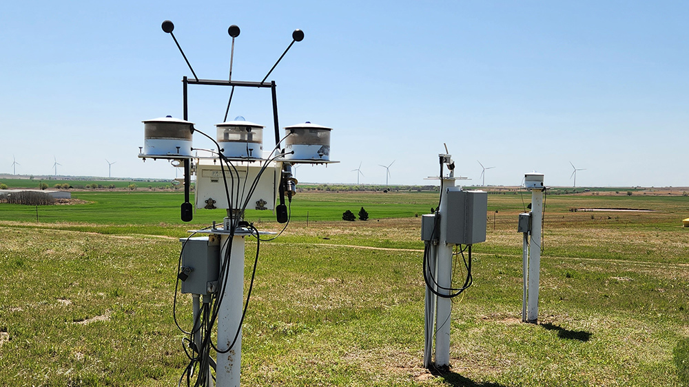 ARM radiometers operate in a field with a building and wind turbines in the distance.