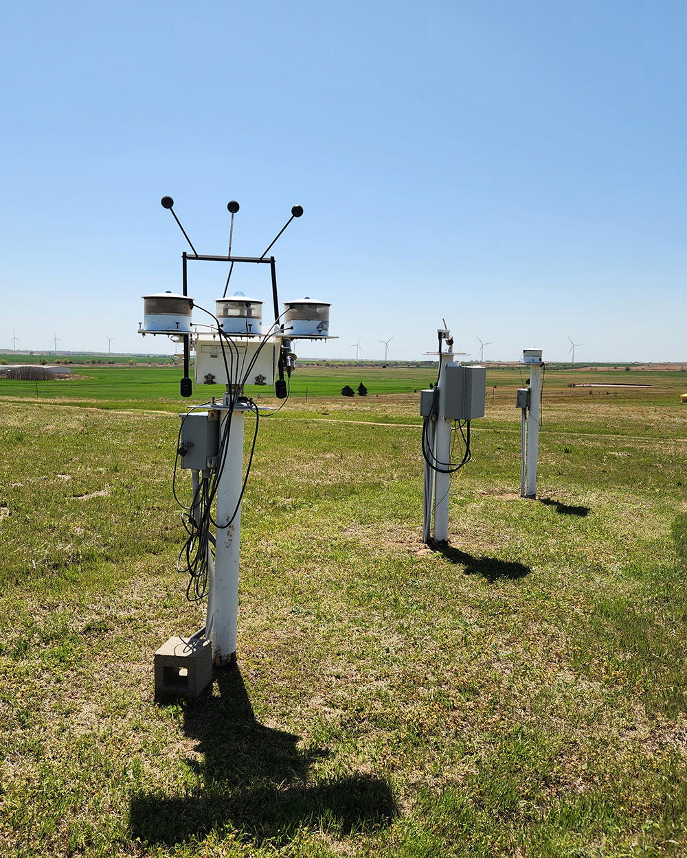 ARM radiometers operate in a field with a building and wind turbines in the distance.