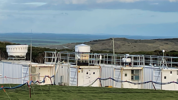 A closeup shot of ARM radars and lidars with grass in front and a rocky hillside in the background