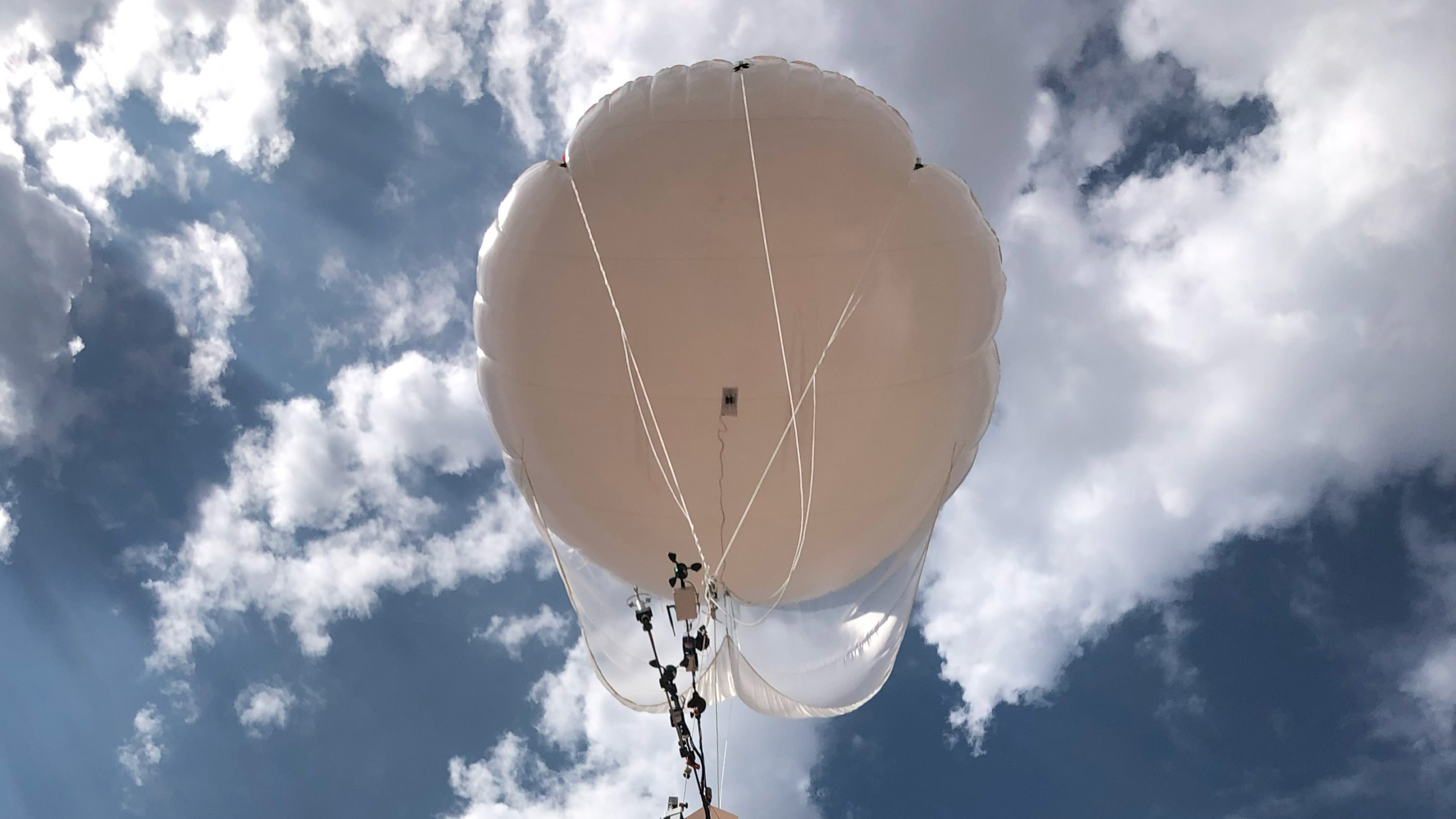 A tethered balloon carries instruments aloft under a cloud-filled sky.